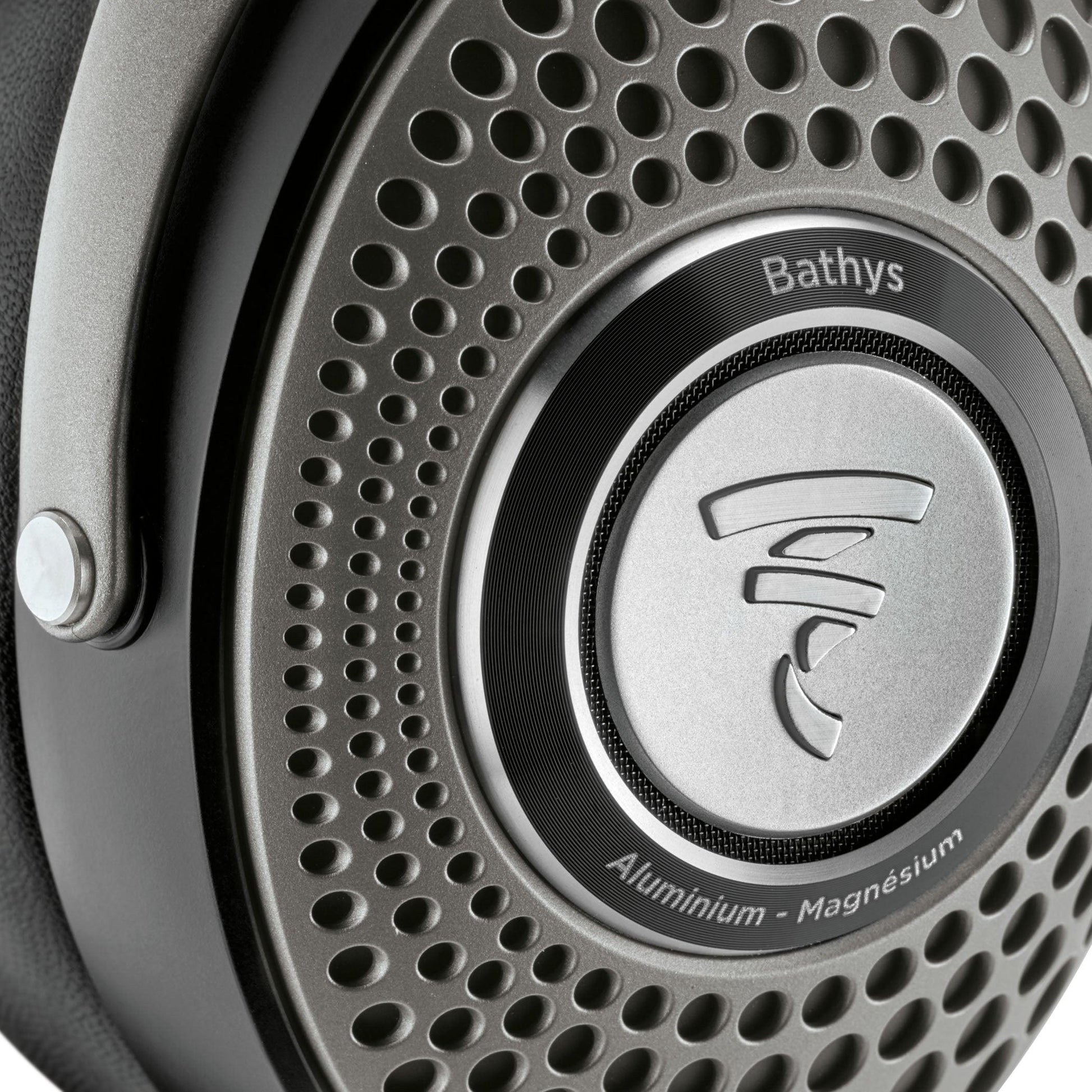 Close-up of the Focal Bathys headphone ear cup by Focal, featuring a perforated metallic grille with the Focal logo, and “Bathys” plus “Aluminium - Magnesium” engraved around it.