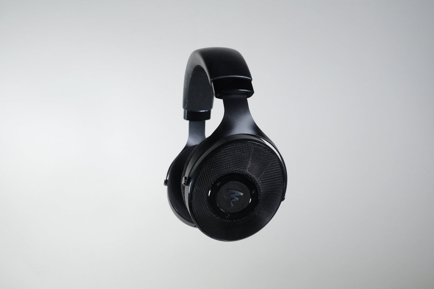 Focal Elex headphones by Focal are shown suspended against a plain light gray background, featuring black over-ear cups with a textured finish and center logo, echoing their modern design and renowned sonic quality.