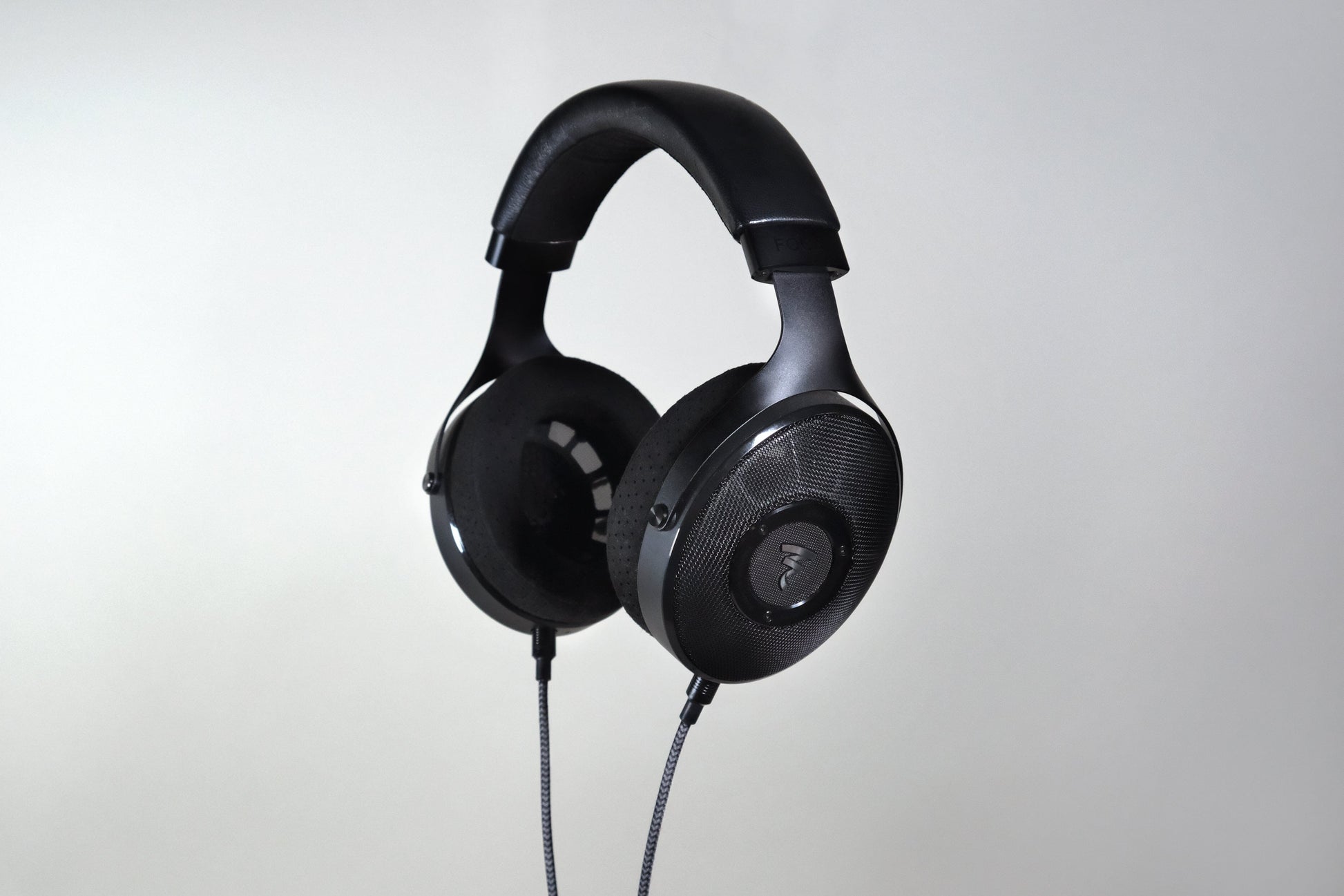 The Focal Elex Headphones by Focal are black over-ear dynamic headphones with a padded headband and coiled cable, shown against a light gray background, crafted for sonic perfection.