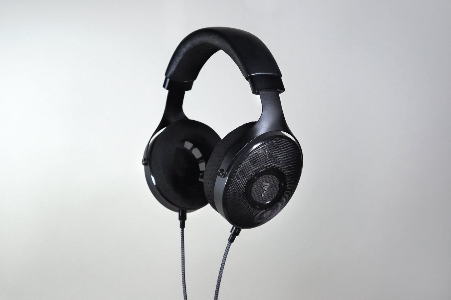 The Focal Elex Headphones by Focal are black over-ear dynamic headphones with a padded headband and coiled cable, shown against a light gray background, crafted for sonic perfection.