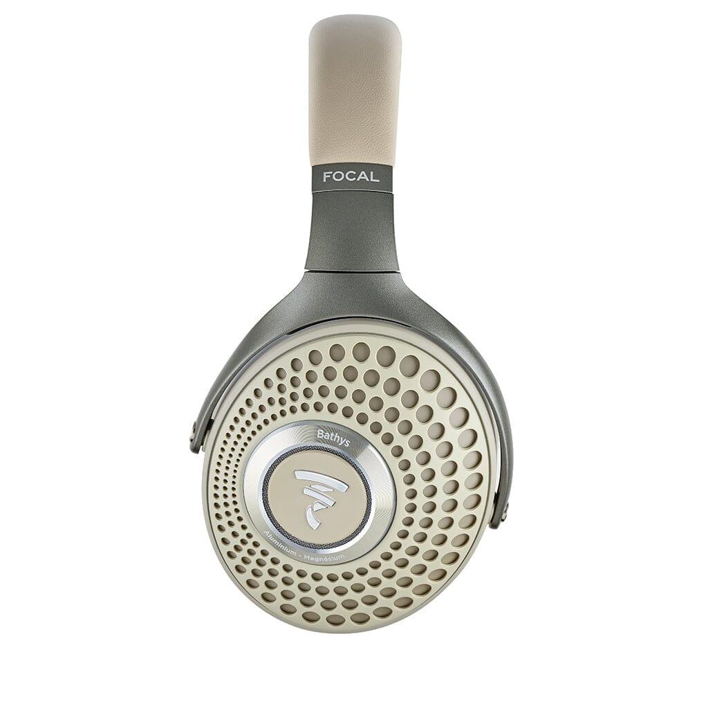 A close-up of the Focal Bathys headphone earcup by Focal, finished in beige and gray, showcases a circular, perforated grille with the Focal logo at its center.