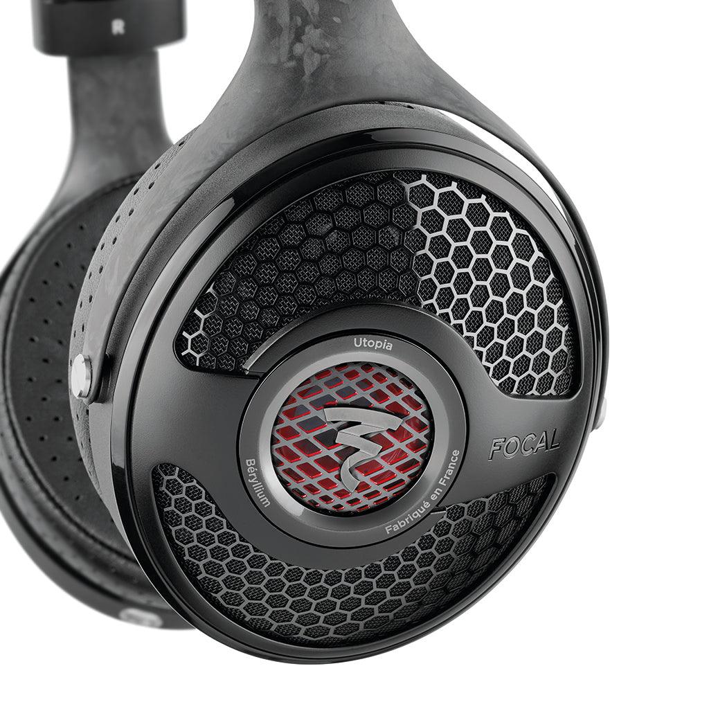 Close-up of the Focal Utopia 2022 headphone earcup, showing a black honeycomb grille with silver accents and a central red logo—highlighting its premium design and acclaimed sound quality.
