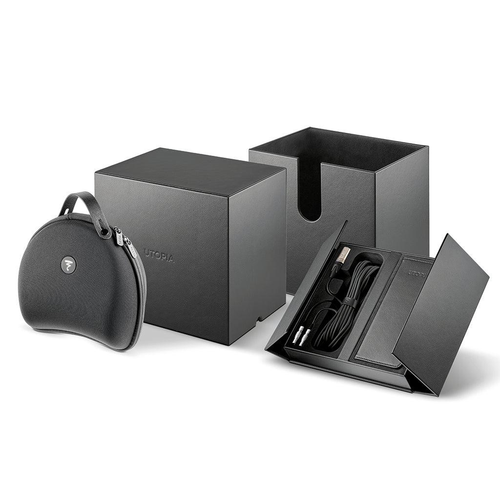A black luxury Focal Utopia 2022 headphone case, a matching black box, and an open folder displaying audio cables are arranged on a white background, showcasing the premium design and quality of Focal’s flagship headphones with minimal branding.