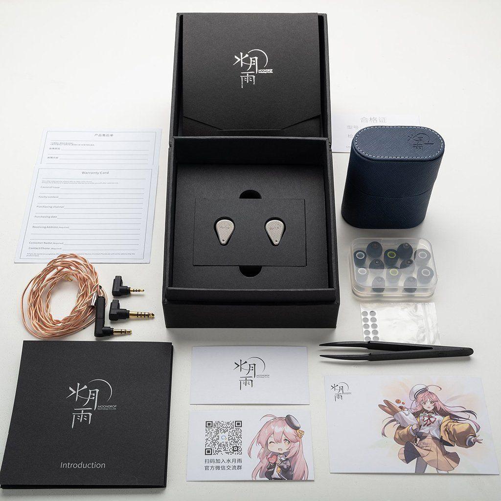 The Moondrop Variations Tribrid In-Ear Headphones by Moondrop come in a black box with cables, ear tips, a black case, tweezers, manuals, warranty cards, and an anime-themed illustrated card—all neatly arranged on a white surface.