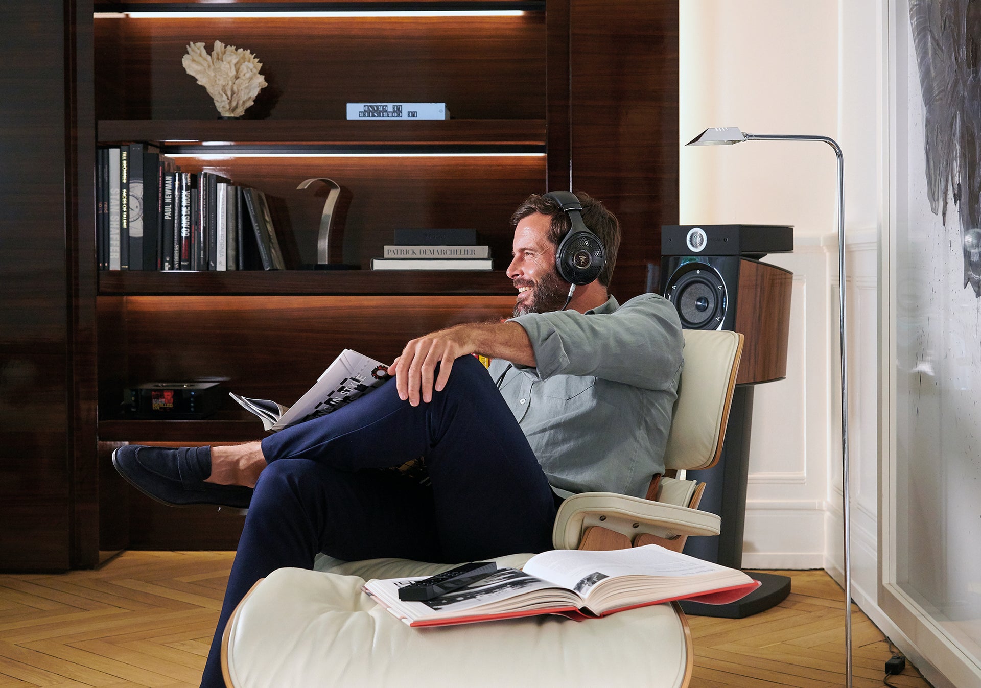 Man sitting in lounge chair listening to Focal Utopia headphones with book open